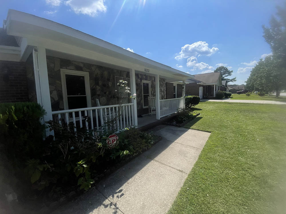 Front lawn view of completed porch roofline, white handrails, and stone accent facade